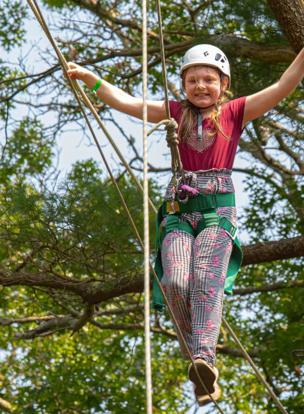 Smiling girl wearing a helmet walking the ropes at Camp Clarks ropes course